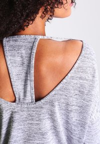 Chemise en tissu texturé gris avec un design à dos ouvert et des bretelles larges, mettant en valeur un look superposé.