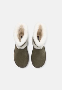 Bottes de chevilles en daim vert olive avec un revers en fausse fourrure crème et des détails de couture le long de la semelle. Doublure intérieure douce pour un confort supplémentaire.