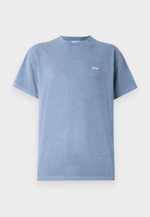 Light blue cotton T-shirt with a round neckline, short sleeves, and a small white logo "obey" on the left chest area. Smooth texture.
