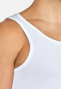 Weißes Tanktop aus glattem Stoff, mit breiten Trägern und enganliegendem Design, mit einem sauberen Abschluss am Halsauschnitt und den Armlöchern.