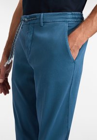Blaue Hose mit elastischem Bund und Kordelzug. Verfügt über seitliche Taschen und ein glattes, leicht strukturiertes Gewebe. Lässige Passform.