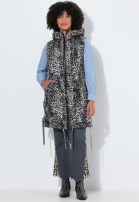 Gepolsterte Weste im Leopardenmuster mit Kapuze, Frontreißverschluss und verstellbarem Kordelzug. Über einem blau gestreiften Hemd und grauen Schlaghosen getragen.