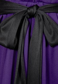 Ceinture en tissu noir nouée en un nœud papillon autour d'un vêtement matelassé violet ou d'une surface en tissu.