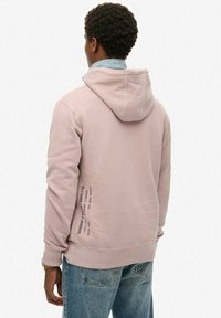Hoodie in lichtroze, met een relaxte pasvorm, ribgebreide manchetten en een zijlabel. Draagt met lichtblauwe denim jeans.