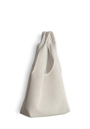 Grand sac fourre-tout blanc perforé avec deux poignées, présenté suspendu sur un fond blanc.