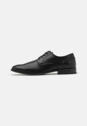 Black leather dress shoe with a pointed toe, lace-up design, subtle brogue detailing, and a smooth finish. Suitable for formal wear.