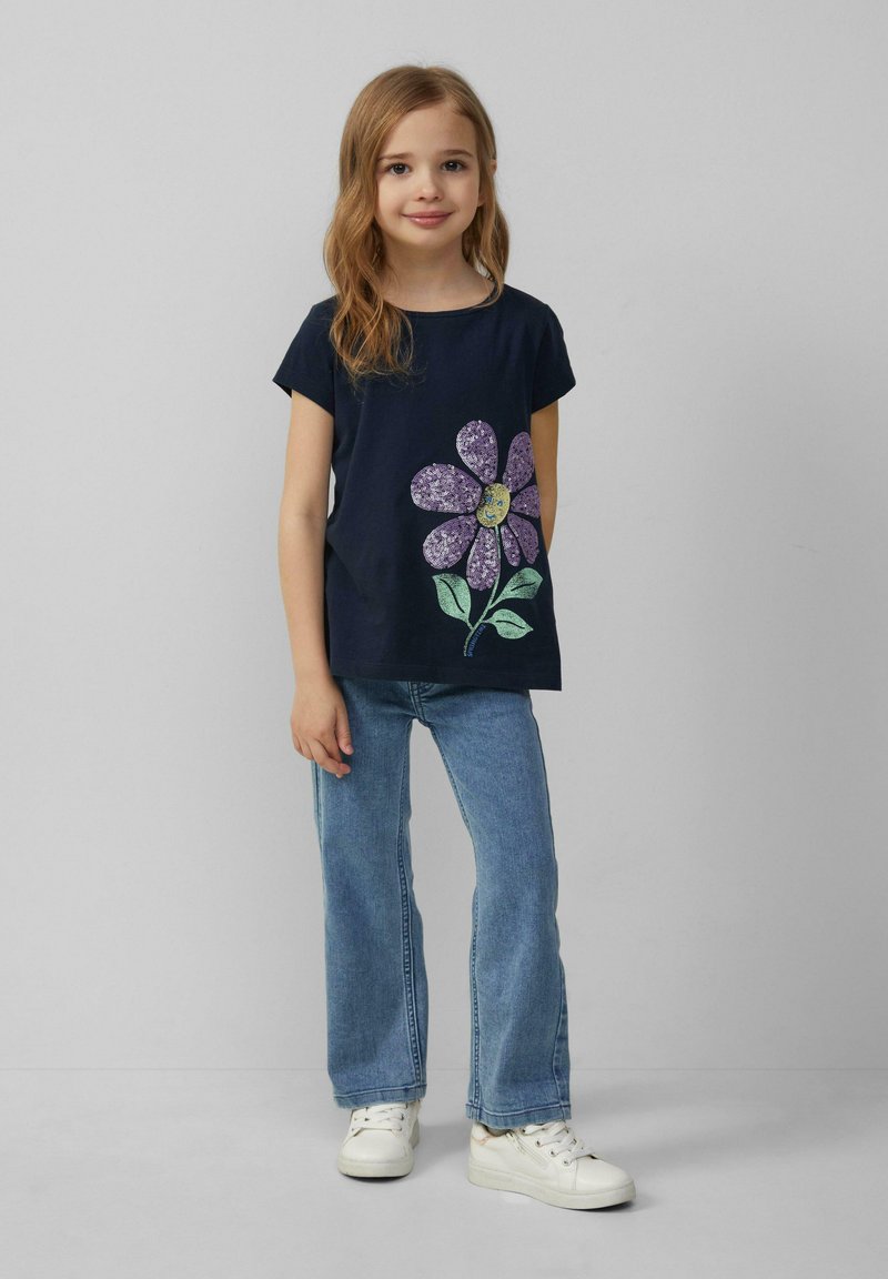 Marineblaues T-Shirt mit floralem Design, das lila Blütenblätter und grüne Blätter zeigt, kombiniert mit hellblauen Jeans und weißen Sneakers.