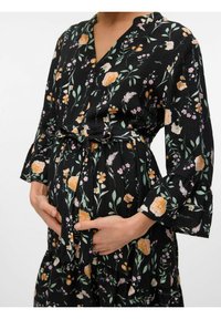 Abito floreale nero con fiori arancioni e rosa. Presenta un design avvolgente, maniche lunghe e un fiocco in vita, drappeggiato su una pancia tondeggiante.