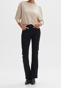 Haut à manches longues beige côtelé associé à un pantalon noir évasé. La tenue présente une coupe décontractée et les deux pièces ont une texture lisse.