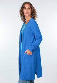 Langer blauer Cardigan aus strukturiertem Material, mit offener Vorderseite, zwei Taschen, gerippten Bündchen und einem gestreiften Hemd darunter. Glattes, leichtes Design.