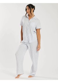 Ljusblå pyjamasset bestående av en kortärmad skjorta med knäppning och ficka samt matchande långa byxor, båda med prickigt mönster och scallopade fållar.