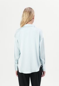 Lys blå silkebluse med en afslappet pasform, lange ærmer, krave og knapmanchetter. Glat tekstur, let buet kant bagpå.