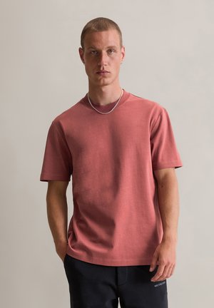 Kurzärmliges T-Shirt mit Rundhalsausschnitt in verblasstem Rosenfarben, aus Baumwolle gefertigt, mit lockerer Passform und subtiler Textur. Minimalistisches Design.