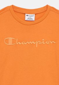 Πορτοκαλί βαμβακερό t-shirt με κεντημένο λογότυπο "Champion" στο μπροστινό μέρος, μέγεθος μικρό για ηλικία 7/8, κατασκευασμένο στο Μπαγκλαντές.