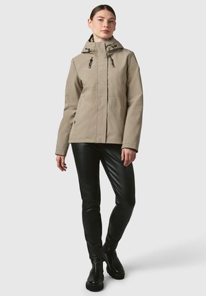 Beige waterproof jacket with a zippered front, adjustable hood, and two front pockets, paired with shiny black leggings and ankle boots.
