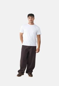 Weißes Baumwoll-T-Shirt kombiniert mit lockeren, dunkelbraunen Hosen und braunen Schuhen. Das Outfit zeichnet sich durch ein entspanntes, lässiges Design aus.