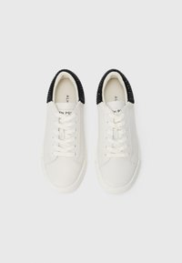 Hvite lavtopp sneakers med hvite snører og svart teksturert detaljering på hælen, sett ovenfra på en hvit bakgrunn.