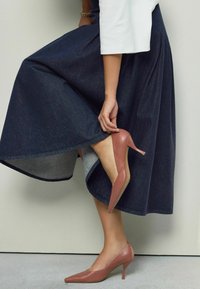 Scarpe con tacco alto e punta affusolata di un delicato rosa, abbinate a una gonna svasata in jeans scuri, con un orlo dalla texture sottile.