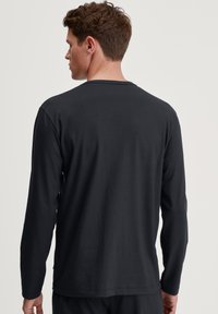 Zwart t-shirt met lange mouwen, gemaakt van zachte stof, met een ronde halslijn, een relaxte pasvorm en eenvoudige stiksels langs de zoom en de manchetten.