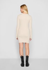 Långärmad beige klänning med en figurnära form, slät textur och minimalistisk design, kombinerad med svarta knähöga stövlar.