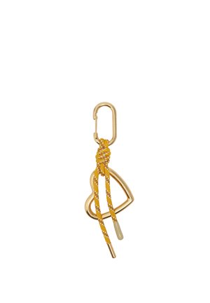 Llavero con mosquetón dorado, con un colgante en forma de corazón abierto y un cordón amarillo anudado con acentos blancos colgando de él.