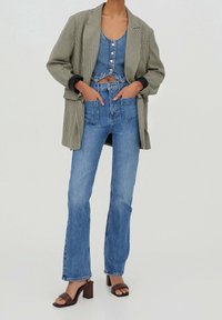 Blazer à carreaux beige et noir porté sur un crop top en denim bleu avec des boutons, associé à un jean évasé bleu taille haute et des sandales à talons carrés marron.