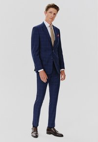 Granatowy, w kratkę, garnitur wykonany z teksturowanej tkaniny, o dopasowanym kroju, z klapami notched oraz różową chusteczką w kieszeni. Uzupełniony jasnym krawatem.