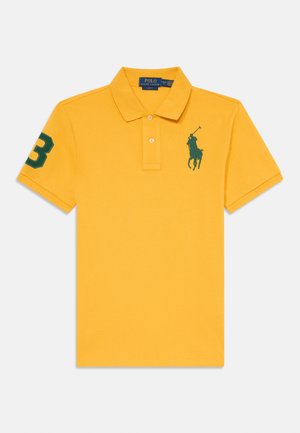 Geltona medvilninė polo marškinėliai su trimis mygtukais, žaliu siuvinėtu polo žaidėjo logotipu ir žalia taisykle 3 ant rankovės.