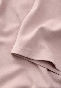 Tessuto rosa chiaro con una trama a coste, che mostra una sezione piegata e l'orlo della manica. Il materiale appare morbido e leggermente elastico.