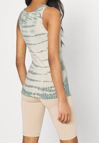 Tanktop in creme und grünem Batikmuster, aus weichem Stoff gefertigt. Kombiniert mit beigen, figurbetonten Radshorts, die eine lässige Passform und einen abgerundeten Saum zeigen.