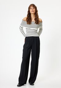 Maglione a righe bianco e nero con scollo off-the-shoulder abbinato a pantaloni larghi neri. Tessuto morbido e vestibilità rilassata.