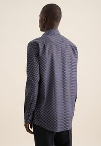 Maglietta navy con motivi a diamante bianchi, maniche lunghe, colletto a punta e orlo curvato. Realizzata in un tessuto liscio e testurizzato.