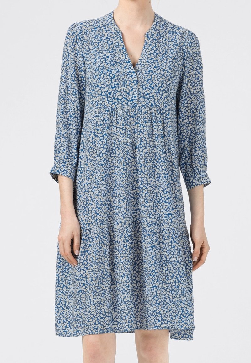 Robe à fleurs bleue avec des motifs blancs. Décolleté en V, manches trois-quarts et coupe décontractée, fabriquée en tissu léger.