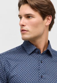 Camicia blu navy con bottoni, caratterizzata da un piccolo motivo floreale, colletto classico e tessuto testurizzato. Bottoni a contrasto sottili completano il design.