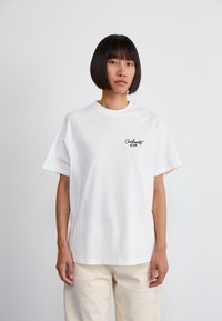 White cotton t-shirt with short sleeves, crew neck, and a small black text logo on the left chest. Relaxed fit, plain design.