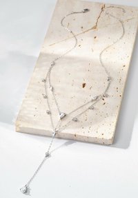 Srebrny naszyjnik łańcuszkowy z akcentami kryształowymi w kształcie kropli i okręgów, o delikatnym wzorze ukazującym warstwową sylwetkę w kształcie litery V.