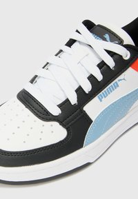 Zwart-witte sneaker met leren bovenkant, geperforeerde neuskap, witte veters, blauwe zijaccenten en zwarte hieldetails.