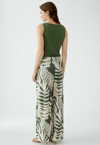 Grünes, geripptes Tanktop, kombiniert mit weit geschnittenen Hosen mit einem cremefarbenen Blattmuster. Das Outfit sitzt oben eng und ist unten locker.