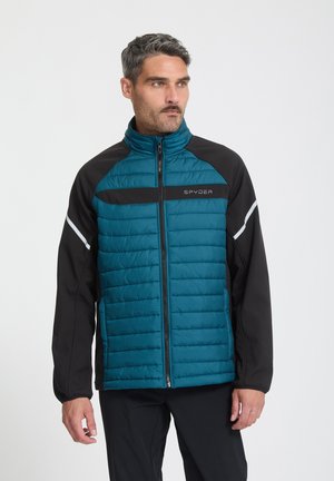 Man draagt een teal- en zwarte Spyder gewatteerde jas met ritssluiting en reflecterende strepen op de mouwen, staand tegen een effen achtergrond.