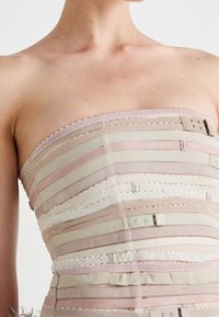 Trägerloses Kleid mit horizontalen Streifen in Beige, Rosa und Weiß. Verfügt über dekorative gewellte Kanten und mehrere Hakenverschlüsse. Glatte Textur.