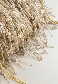 Close-up of beige fabric with gold sequins and clear bead fringe details, accompanied by a gold chain strap on a white surface.
