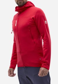 Rote Zip-Jacke mit strukturierter Oberfläche, Kapuze und zwei Reißverschlusstaschen. Besitzt ein Logo auf der oberen linken Brust und enganliegende Ärmel.