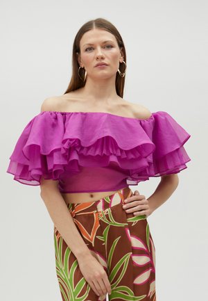 Top fucsia sin mangas con volantes en capas, combinado con pantalones marrones estampados con diseños de hojas coloridas.