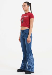 Rød kort�ærmet t-shirt med grafisk design, i kombination med blå flagrende jeans med fisk- og bølgemønstre. Sorte platform sko fuldender looket.