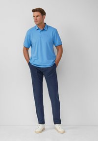Lichtblauwe poloshirt met een kraag, gecombineerd met donkerblauwe broek en witte schoenen. De poloshirt heeft een subtiele logo op de borst.