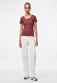 Tumši sarkans ribots T-krekls ar īsām piedurknēm un izgriezumu pie kakla, kombinēts ar baltām platām biksēm un sudraba čībām. Vienkāršs dizains.