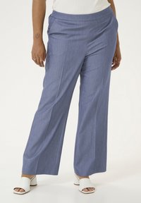 Pantaloni a gamba larga in tessuto azzurro chiaro con una leggera texture. Presentano una vita liscia e pieghe incassate. Abbinati a sandali con tacco bianchi.
