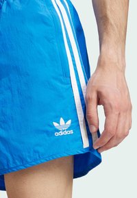 Calções atléticos azuis feitos de um tecido leve, com riscas brancas nas laterais e um logótipo da Adidas bordado perto da bainha.