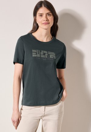 T-shirt en coton vert foncé à manches courtes, avec un imprimé graphique géométrique en vert clair portant la phrase "TROUVEZ VOTRE PAIX INTÉRIEURE."
