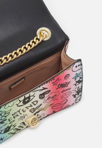 Schwarze Lederhandtasche mit goldener Kettendetails; das Innere verfügt über einen bunten grafischen Druck mit Kritzeleien und Mustern sowie einem glatten braunen Futter.